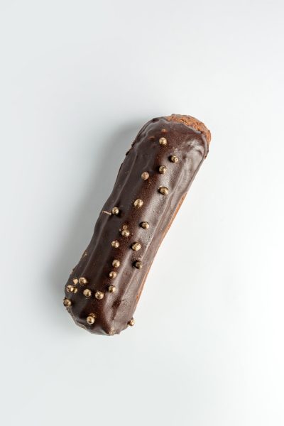 top view of brown eclair garnished with chocolate and golden beads